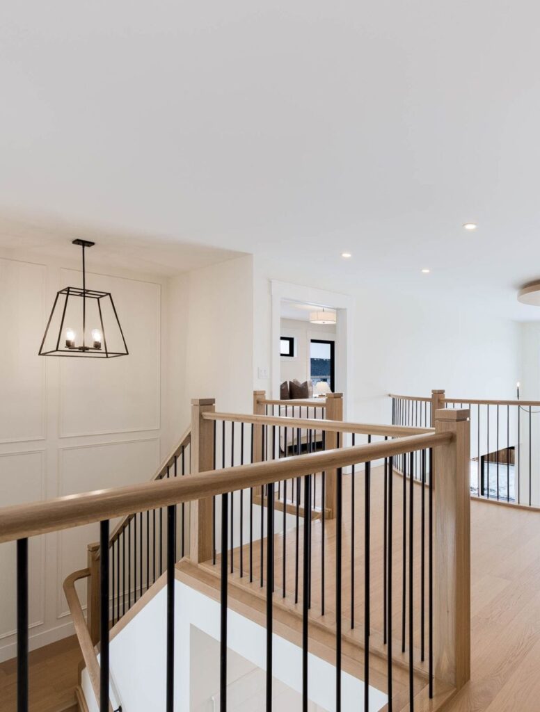 Upper-floor landing with wood handrail and black metal balusters overlooking a bright interior