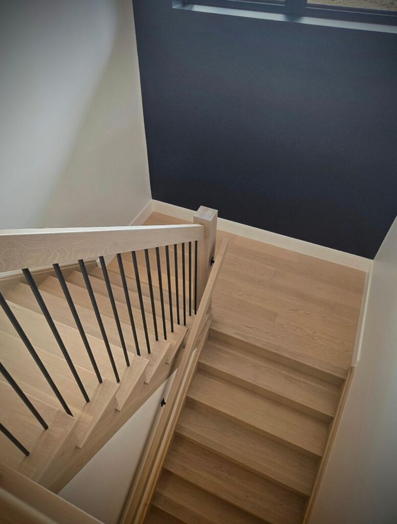 Light wood staircase with black metal balusters beside a dark accent wall